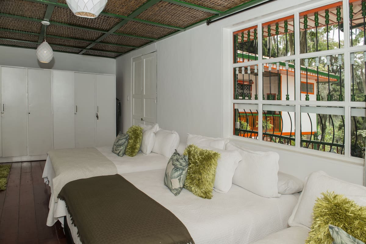 A bedroom with a large bed, white walls, and a window with a view of greenery.