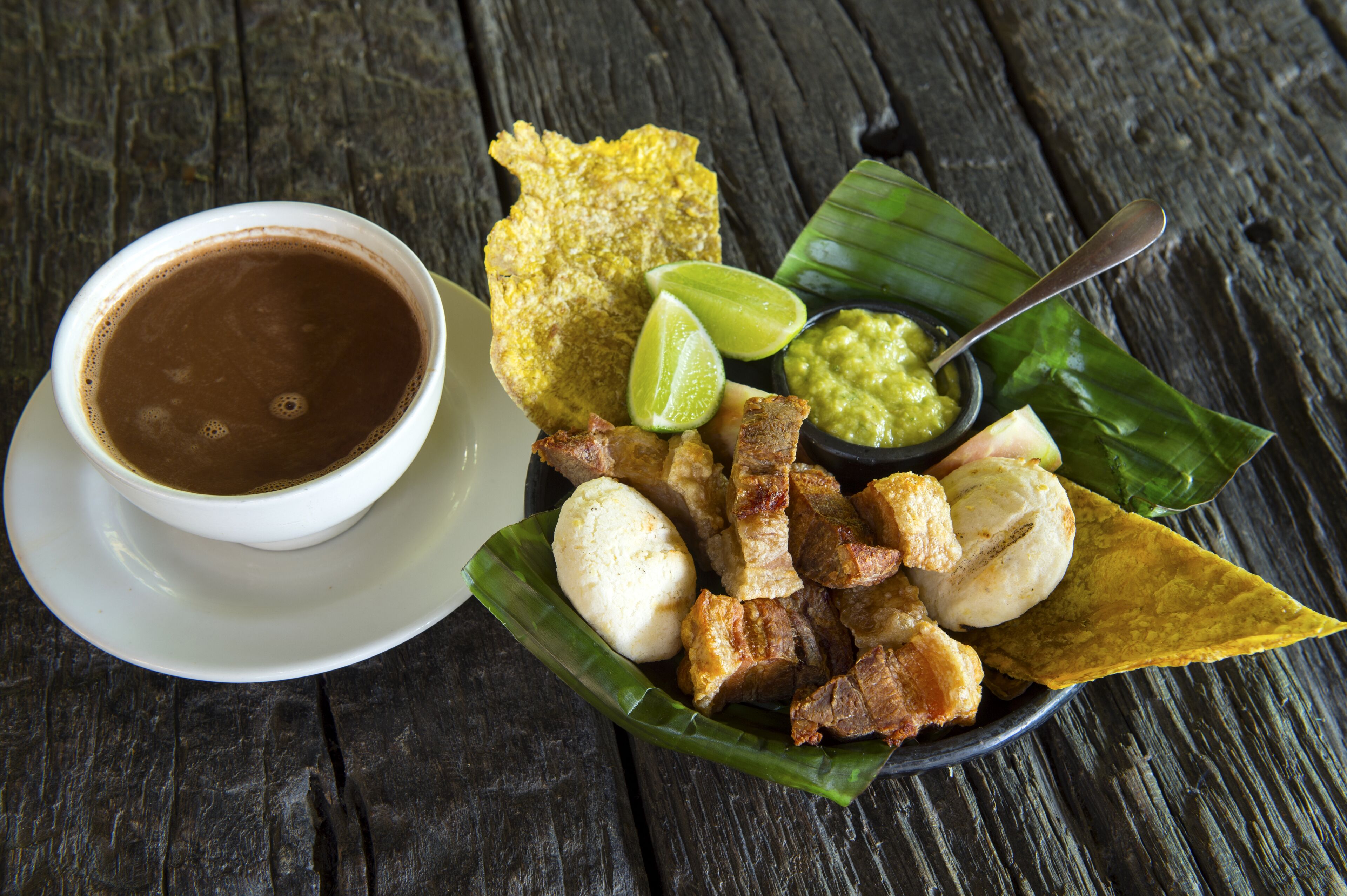 A meal consisting of fried items, a cup of coffee, and a small bowl of sauce, served on a wooden table.