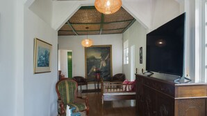 A spacious living room with a high ceiling, a large painting, a television, and a wooden cabinet. - Hacienda Charrascal Coffe Farm (Manizales)