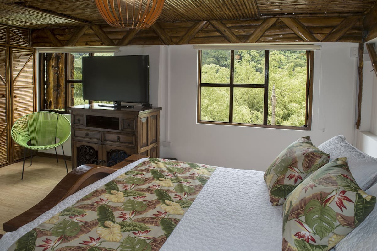 A bedroom with a bed, a television, a window with a view of trees, and a chair.