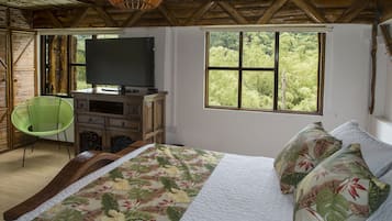 Un dormitorio con una cama, televisión, ventana con vistas a árboles y una silla.