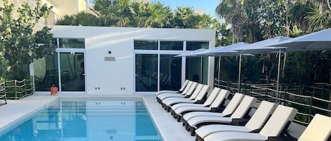 A pool area with lounge chairs and a table, surrounded by glass doors and palm trees.