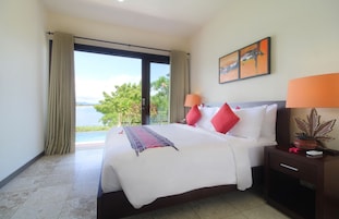 Habitación de hotel con cama, mesita de noche, lámpara, un cuadro y vistas al exterior.