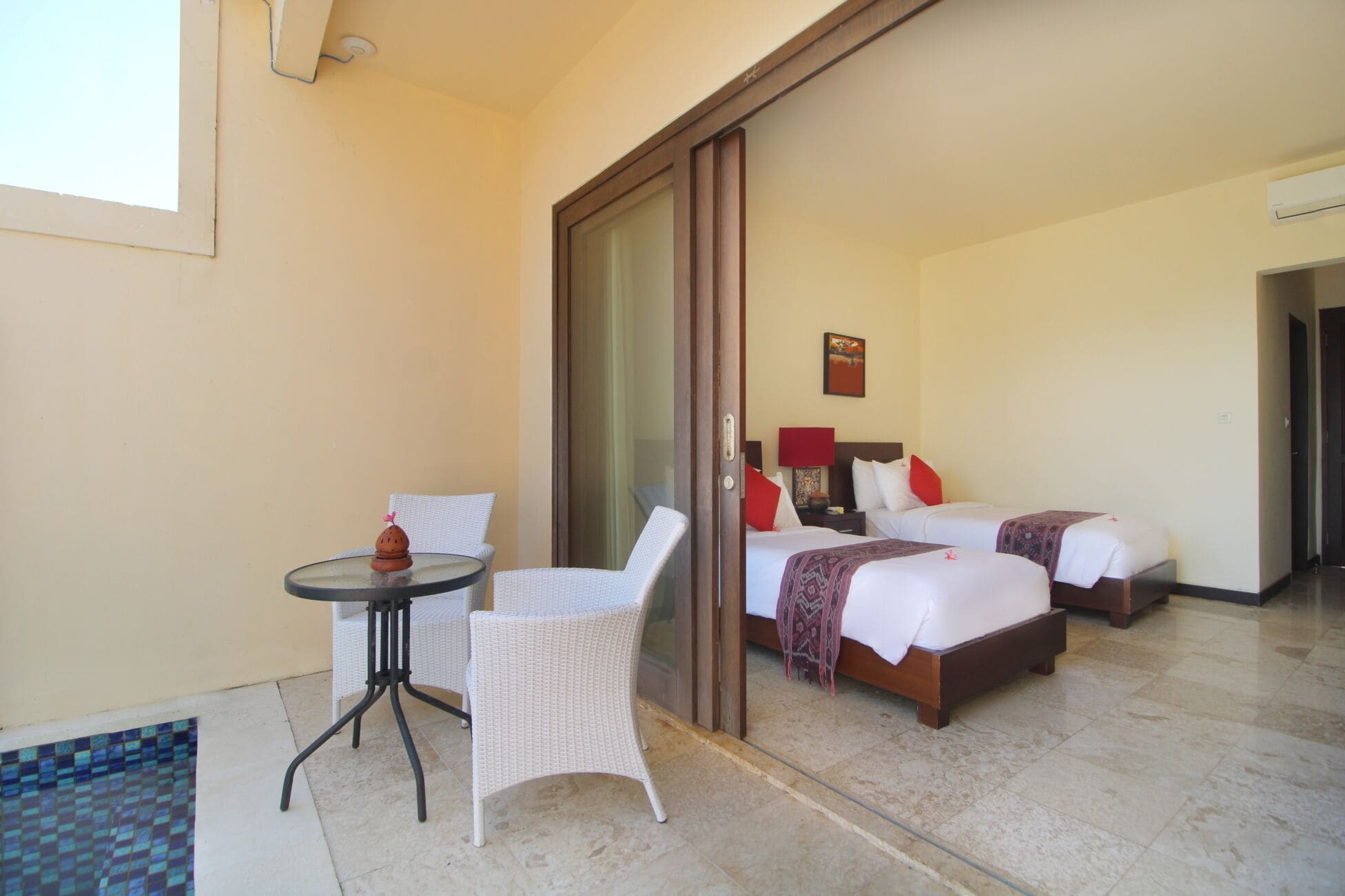A hotel room with two beds, a small table with chairs, a sliding glass door, and a view of the pool area.