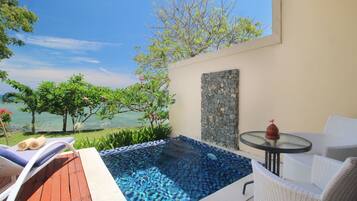 A private outdoor pool area with a view of the sea, a stone wall, and a small table with a decorative item.