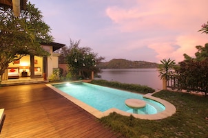 Un hotel con piscina, terraza de madera y vista al lago al anochecer.