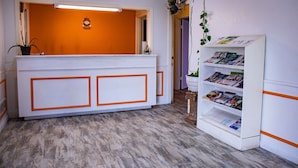Un espace d’accueil avec un comptoir de réception blanc, un mur orange et un présentoir à magazines.