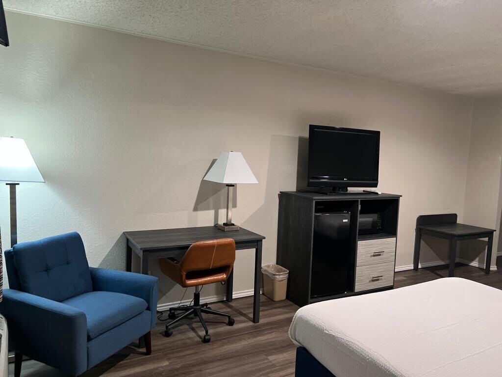 Una habitación de hotel con una cama, un escritorio con una silla, un televisor en un mueble y dos lámparas.