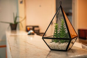 Un terrarium géométrique en verre, contenant une plante et des petits galets blancs, posé sur une surface en marbre.