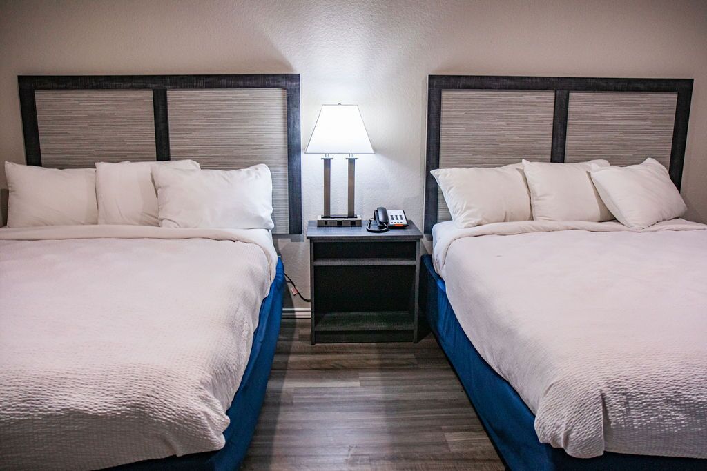 A hotel room with two beds, a nightstand with a lamp, and a phone.