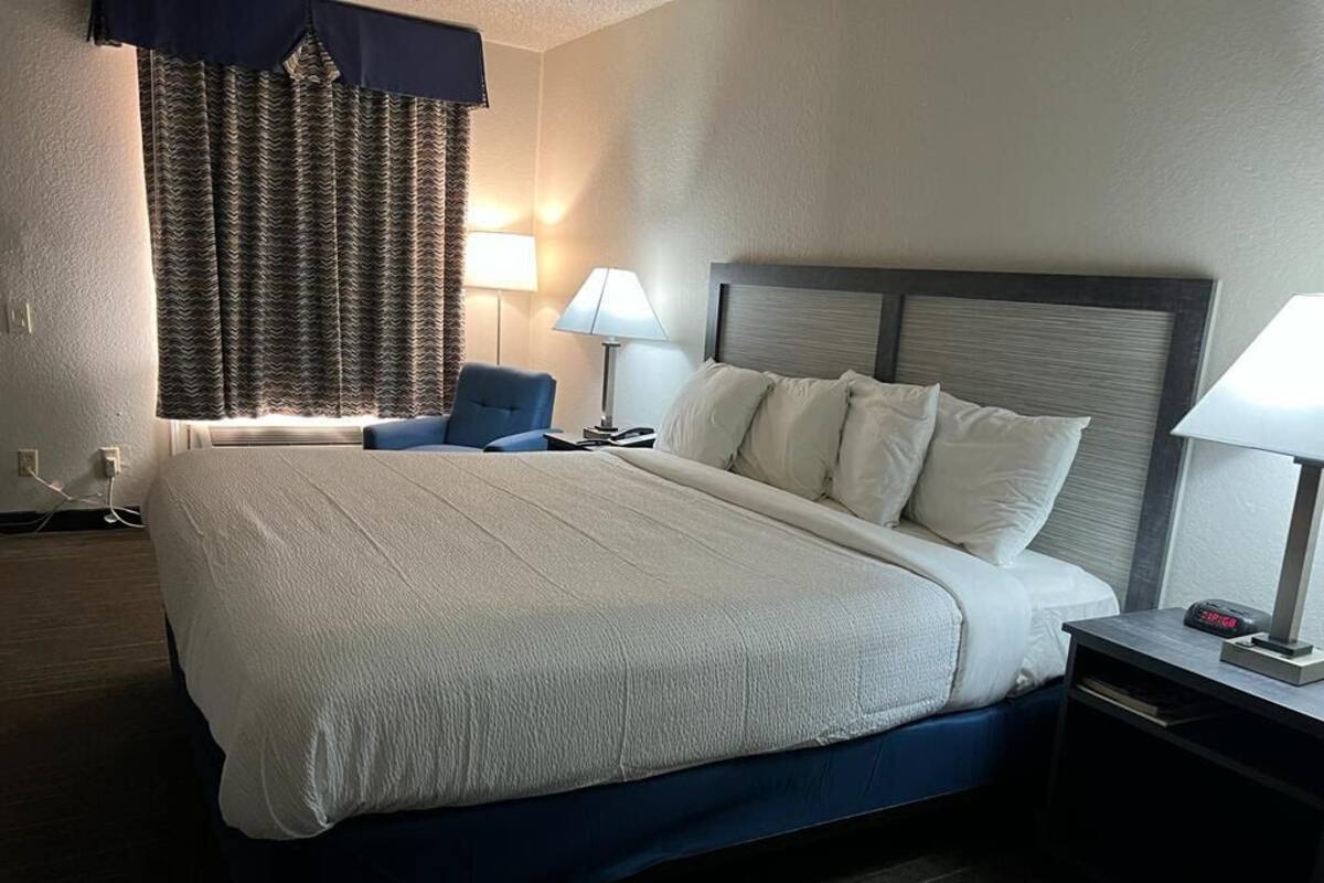 A hotel room with a large bed, two bedside tables, a chair, and a window with curtains.