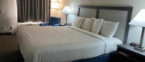 Quarto de hotel com uma cama grande, duas mesas de cabeceira, uma cadeira e uma janela com cortinas.