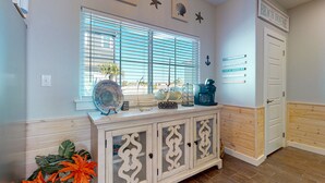 Une pièce avec une fenêtre, un meuble contenant des objets décoratifs et une porte sur laquelle est inscrit « MAISON DE PLAGE ».