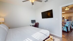 Um quarto com uma cama, uma escrivaninha com computador, uma televisão e um ventilador de teto.