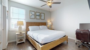 Une chambre à coucher bien rangée, avec un lit en bois, un ventilateur de plafond, une table de chevet avec une lampe et un téléviseur.
