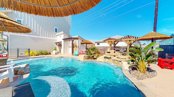 A swimming pool with a stone waterfall feature, surrounded by lounge chairs and umbrellas.
