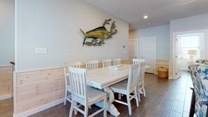 Un espace repas comprenant une grande table et des chaises blanches, un élément décoratif mural et un lambris en bois sur les murs.