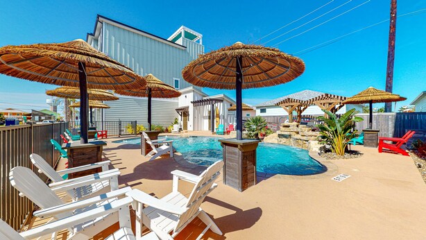Un jardin avec une piscine, des chaises longues et des parasols en chaume.