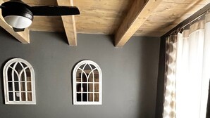 Una camera da letto con un letto, due finestre ad arco, una ventola a soffitto e una finestra con tende.