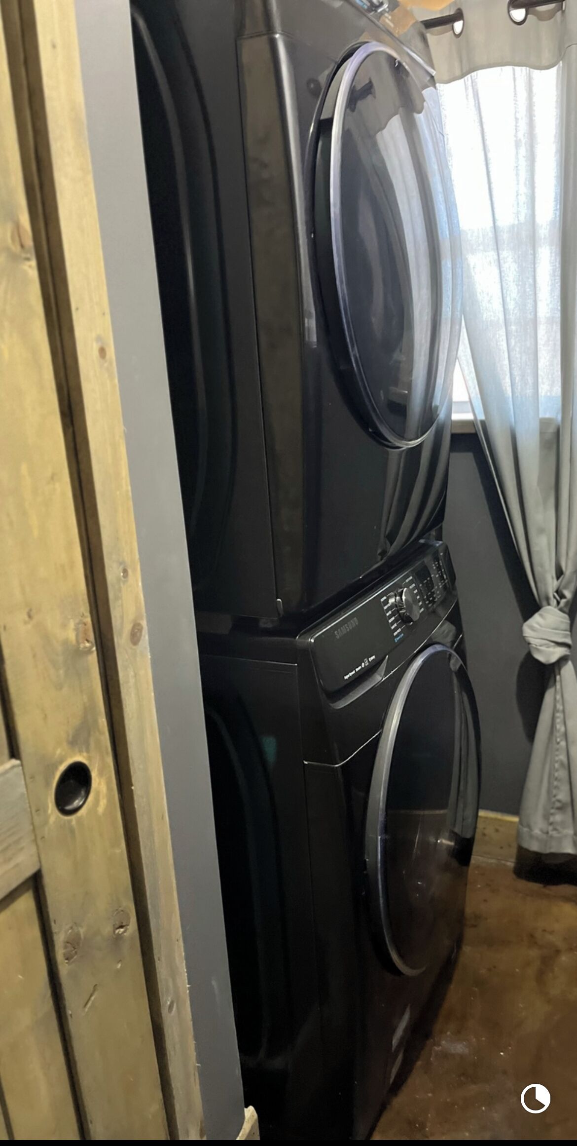 Lavadora y secadora apiladas en una habitación con puerta de madera y cortina.