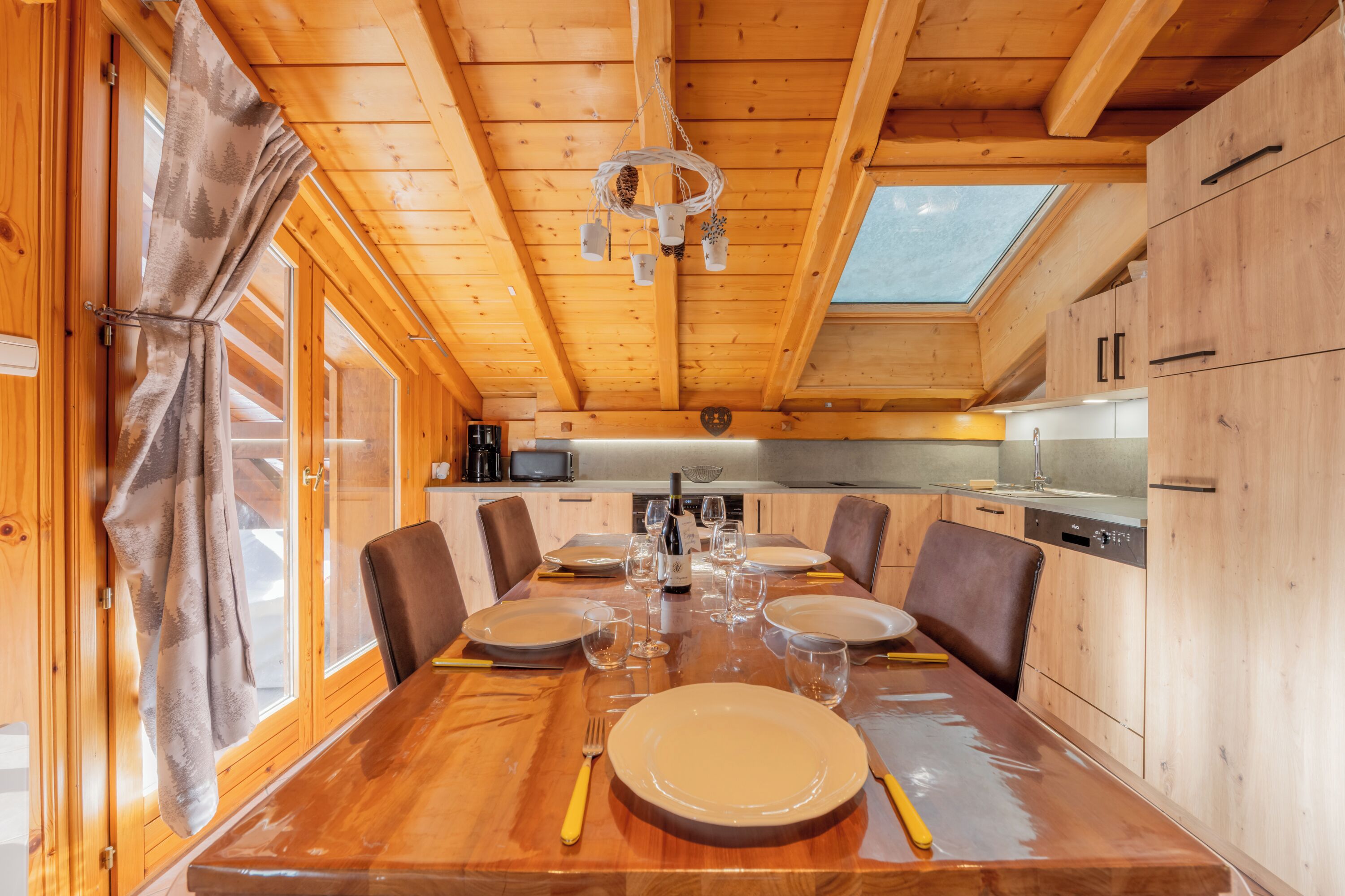 Een houten eettafel gedekt voor zes personen, met borden, bestek en wijnglazen.