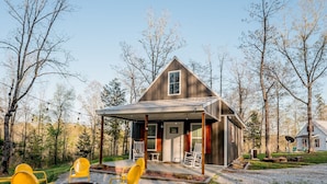 A rustic cabin with a porch, surrounded by trees and gravel paths.