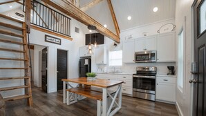 A modern kitchen with white cabinetry, stainless steel appliances, and a wooden dining table.