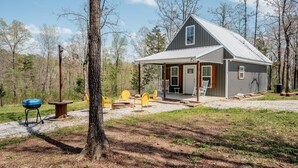 A cabin with a porch, outdoor seating, and a grill area.