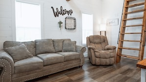 A spacious living room with a wooden ceiling, a leather sofa, a recliner, and a ladder.