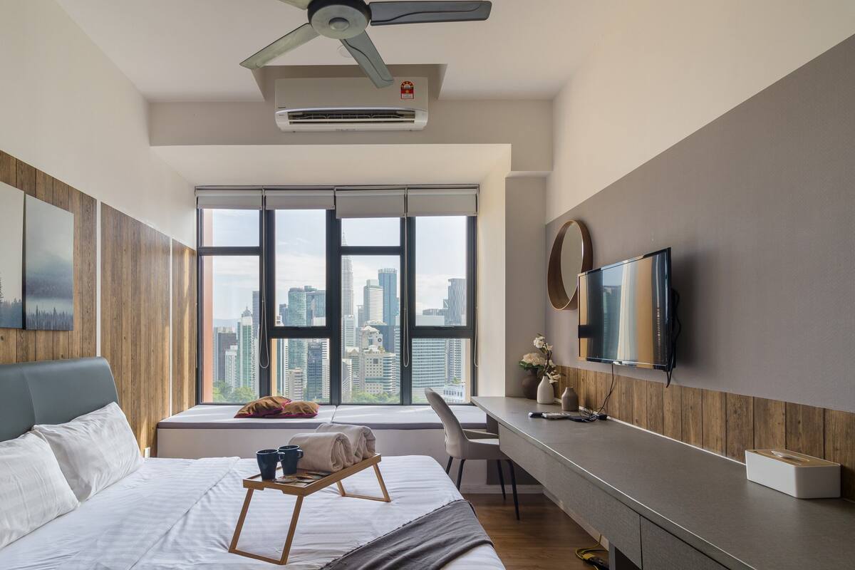 Une chambre moderne avec un grand lit, un bureau et une vue sur le paysage urbain, grâce à de grandes fenêtres.