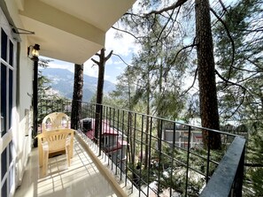 A balcony with a wooden chair, a small table, and a railing overlooking a mountainous landscape with trees.