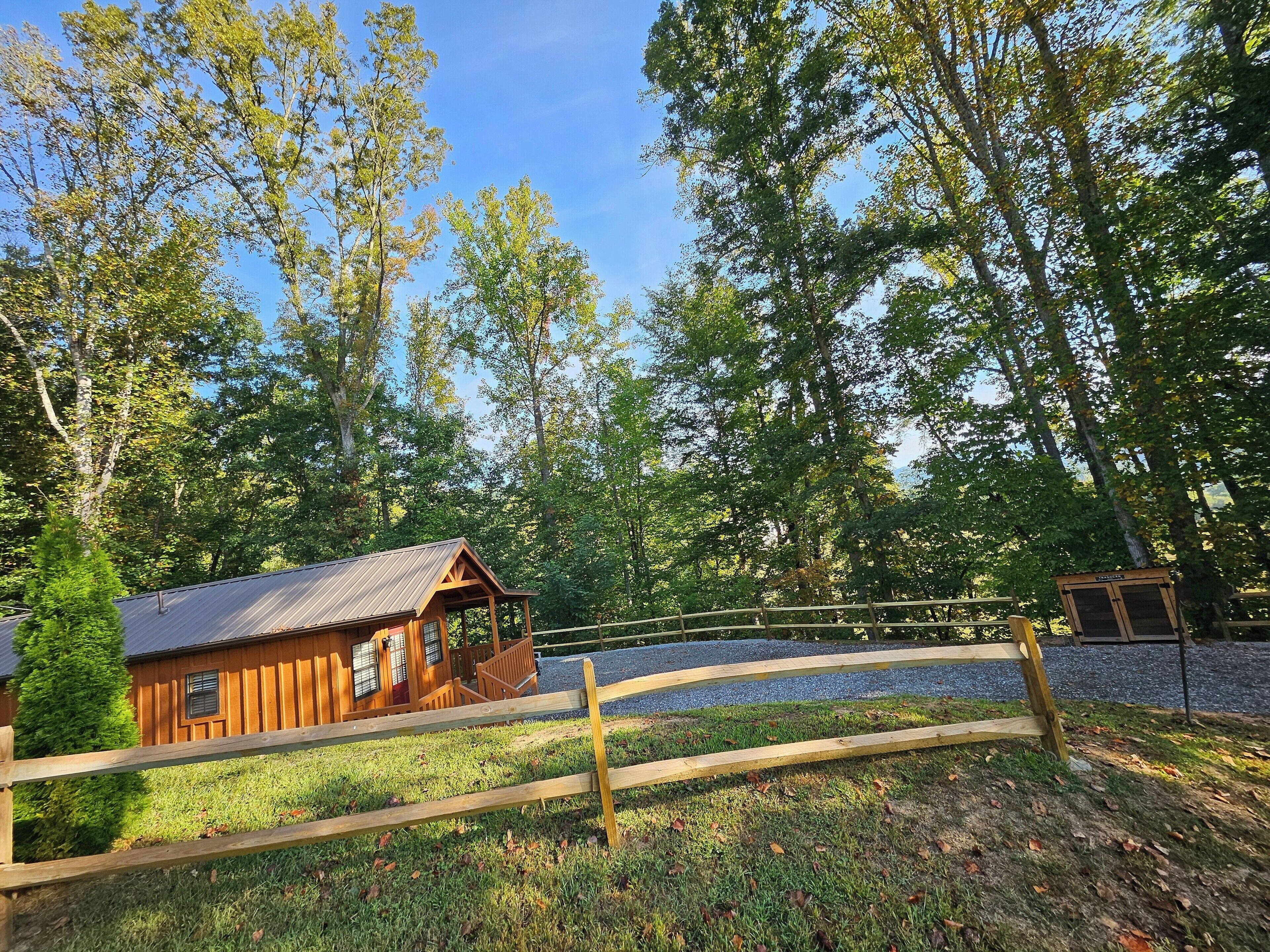 A wooden cabin with a metal roof, surrounded by a wooden fence and trees.