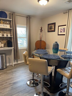 Un coin repas avec une table ronde en verre, des chaises de couleur beige, une machine à café et un violoncelle accroché au mur.