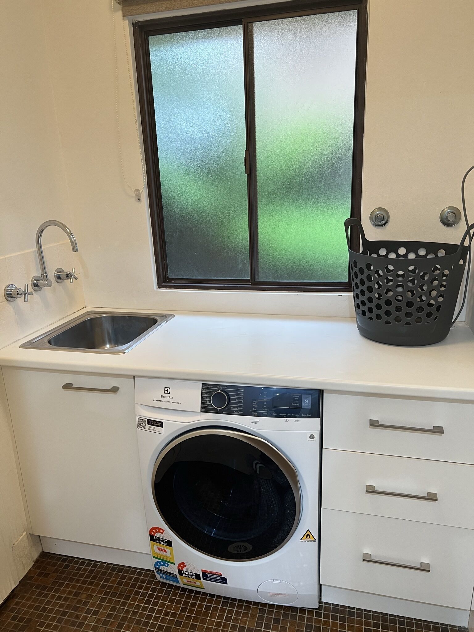 A compact laundry area with a washing machine, a sink, and a window with frosted glass.