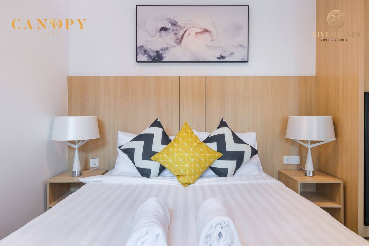 Een hotelkamer met een bed, twee nachtkastjes met lampen, een houten hoofdbord en een lijst met een abstract schilderij aan de muur.