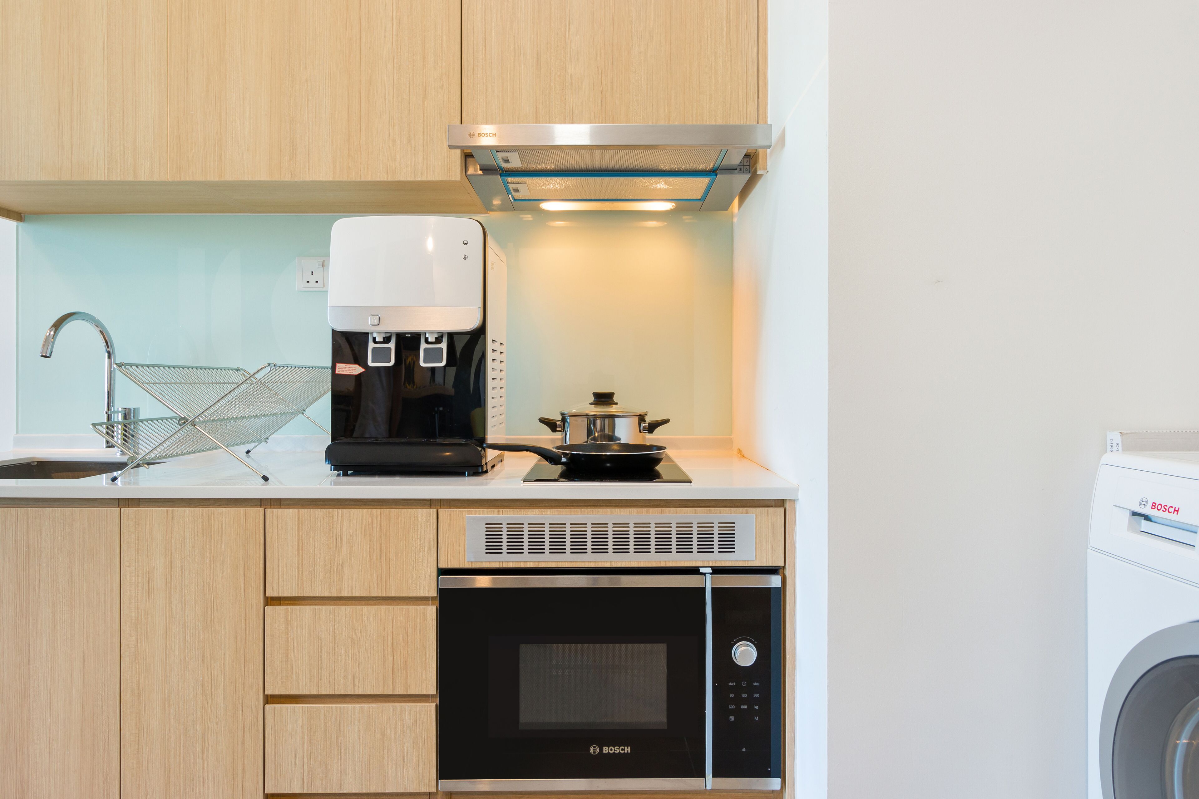 Une cuisine compacte équipée d’une machine à café, d’un four à micro-ondes et d’une petite cuisinière de la marque Bosch.