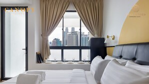 Een hotelkamer met een groot bed, uitzicht op de stad door een raam en een lamp aan de muur.
