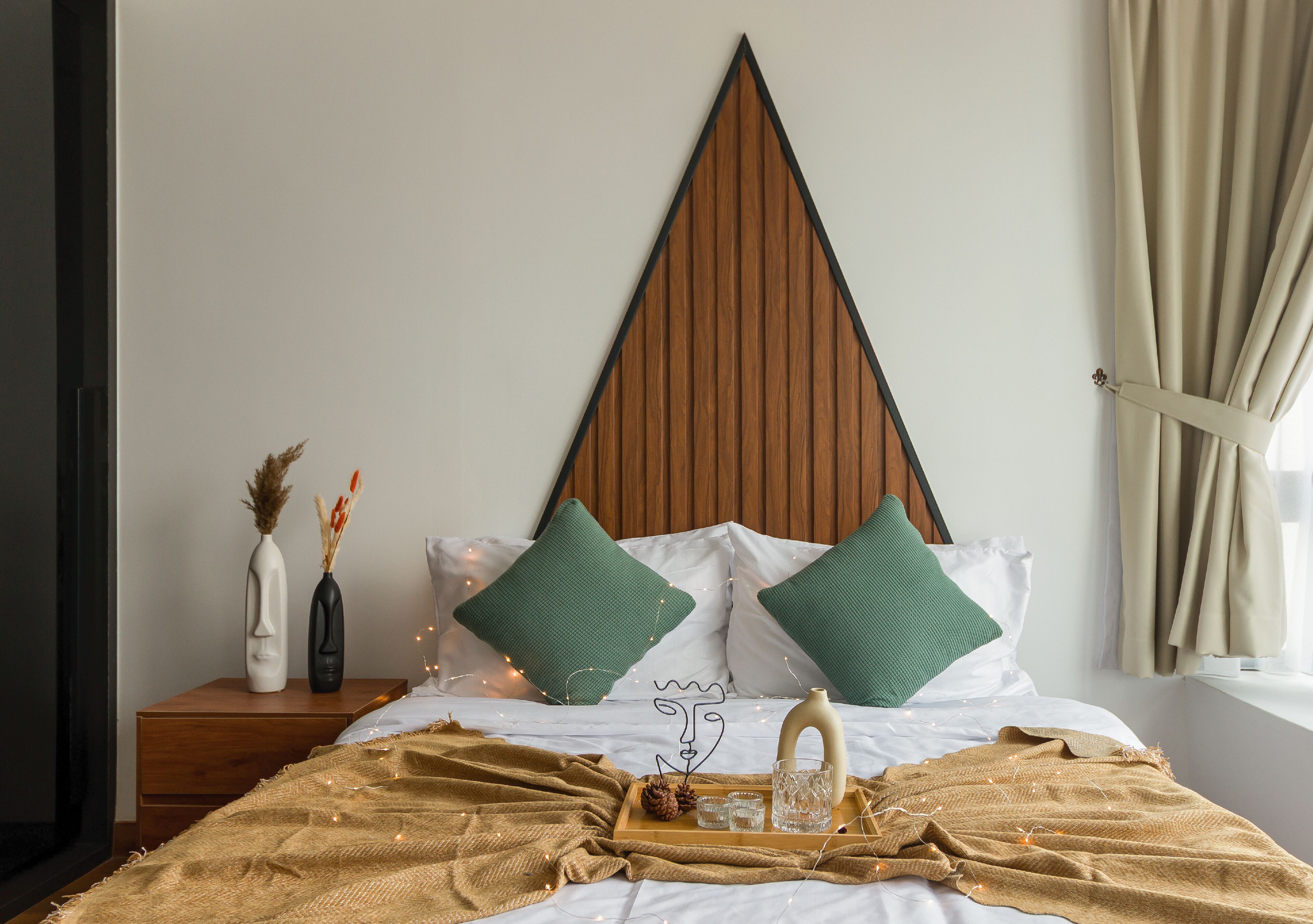 Ein ordentlich bezogenes Bett mit einem Holz-Kopfteil, zwei grünen Kissen und einem Nachttisch mit Dekoration.