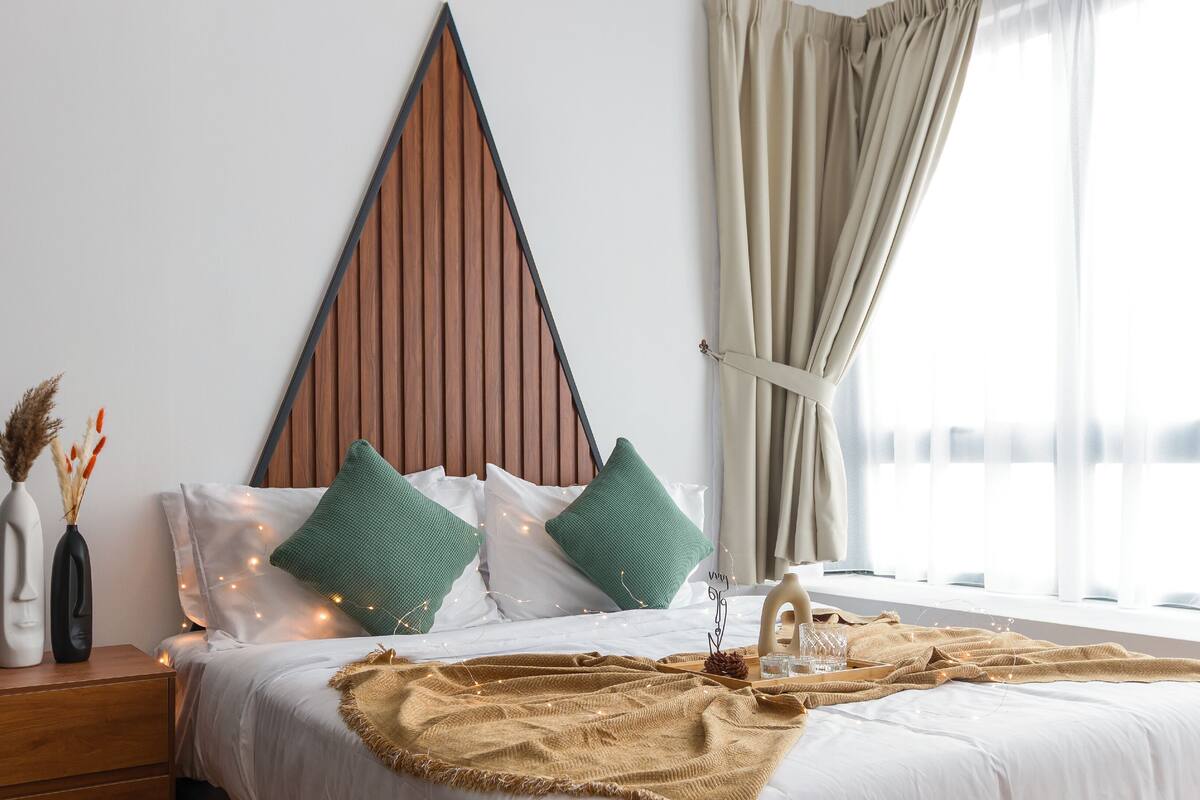 Een netjes opgemaakt bed met witte lakens, groene kussens en een bruine plaid.