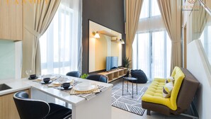 Een moderne woonkamer met een bank, een eethoek met een tafel gedekt voor twee personen, en een groot raam met gordijnen.