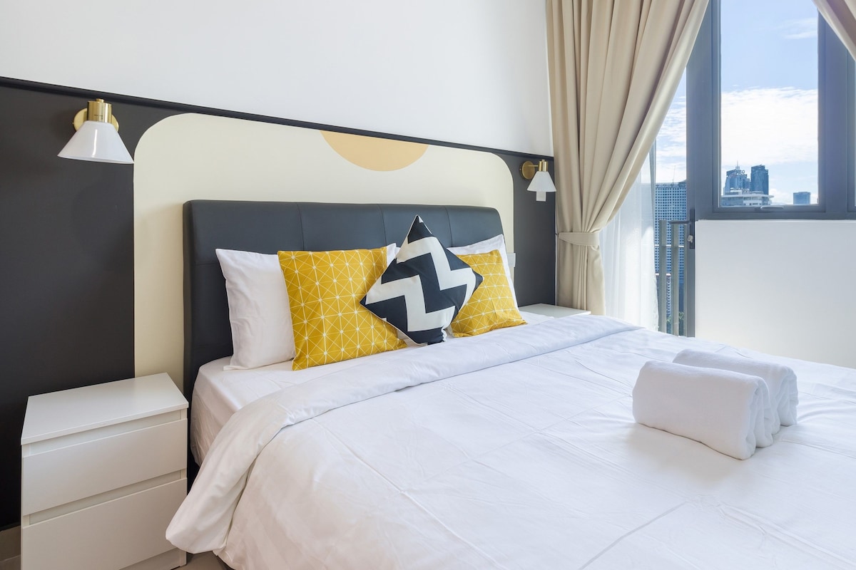 A hotel room with a bed, a nightstand, a window with curtains, and a view of the city.
