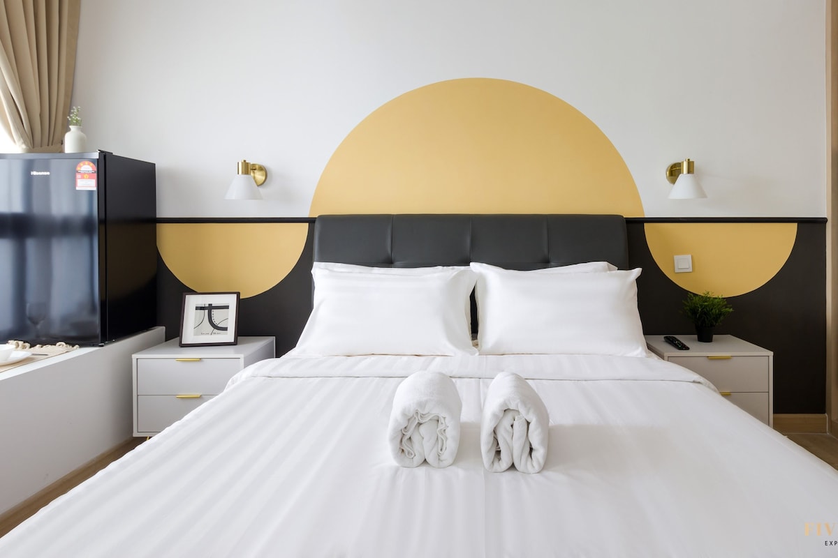 A hotel room with a bed, two bedside tables, a nightstand, a wall-mounted TV, and a large circular design on the wall.