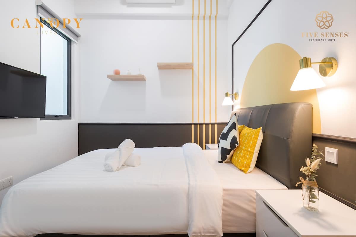 Een moderne hotelkamer met een bed, nachtkastje, lamp en een wandgemonteerde televisie.