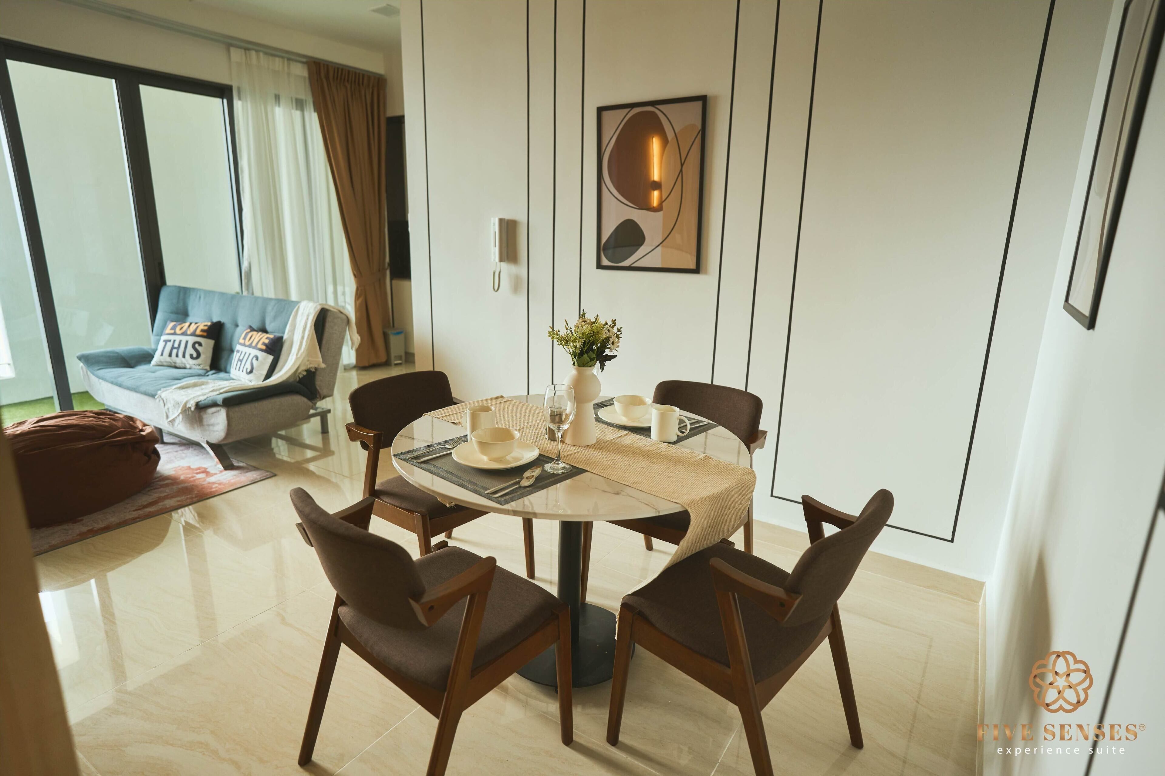 A modern living room with a round dining table, four chairs, a sofa with cushions, a coffee table, and a vase with flowers.