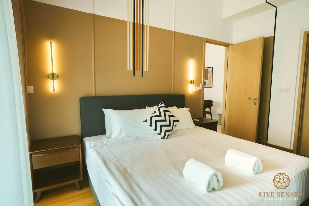 Een opgemaakt bed met witte lakens en twee opgerolde handdoeken, een nachtkastje en wandlampen.