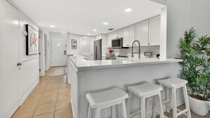 A modern kitchen with white cabinets, a large island with bar stools, a microwave, and a coffee station. - Oceanfront Condominium with Pool. (Saint Simons Island)
