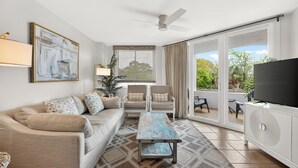 A living room with a sofa, chairs, a coffee table, a TV, and a balcony with a view. - Oceanfront Condominium with Pool. (Saint Simons Island)