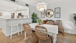 A modern kitchen with white cabinetry, a dining area with wicker chairs, and a central island. - Oceanfront Condominium with Pool. (Saint Simons Island)