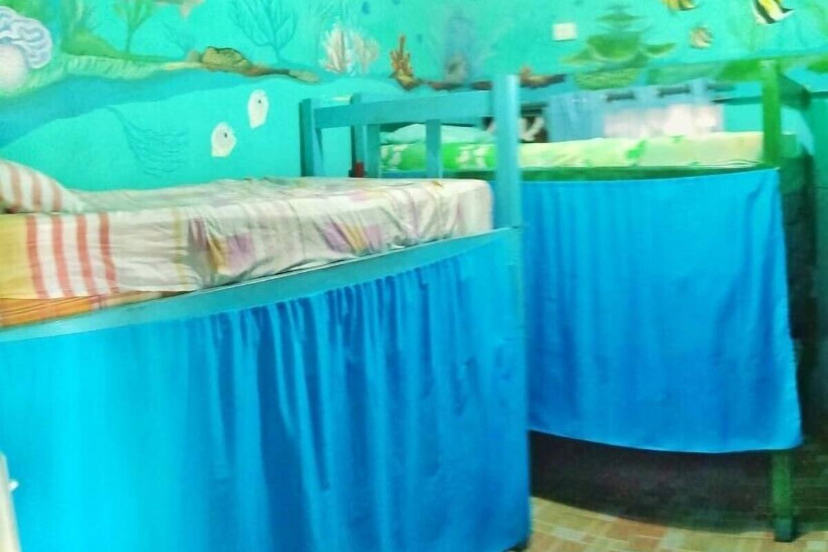 Ein Zimmer mit zwei mit blauen Laken bezogenen Betten, einem Fliesenboden und einer Wand mit Darstellungen von Meereslebewesen.