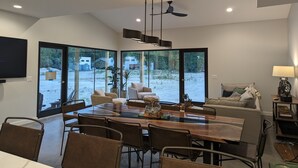 A spacious dining area with a large table and chairs, a ceiling fan, and a view of the outdoors through large glass doors. - Family Friendly Lake Front New Build - 5bdrm + Hot Tub (Stevensville)